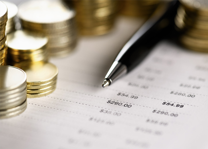 Paper with dollar amounts underneath gold coins and a pen