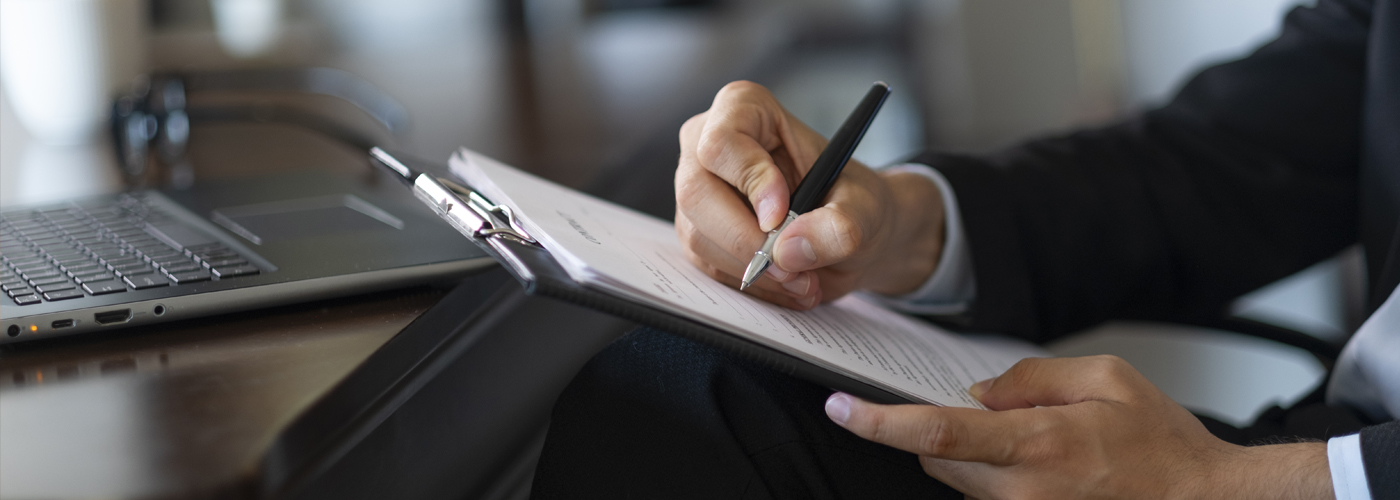 Man sitting at a desk with pad of paper signing it